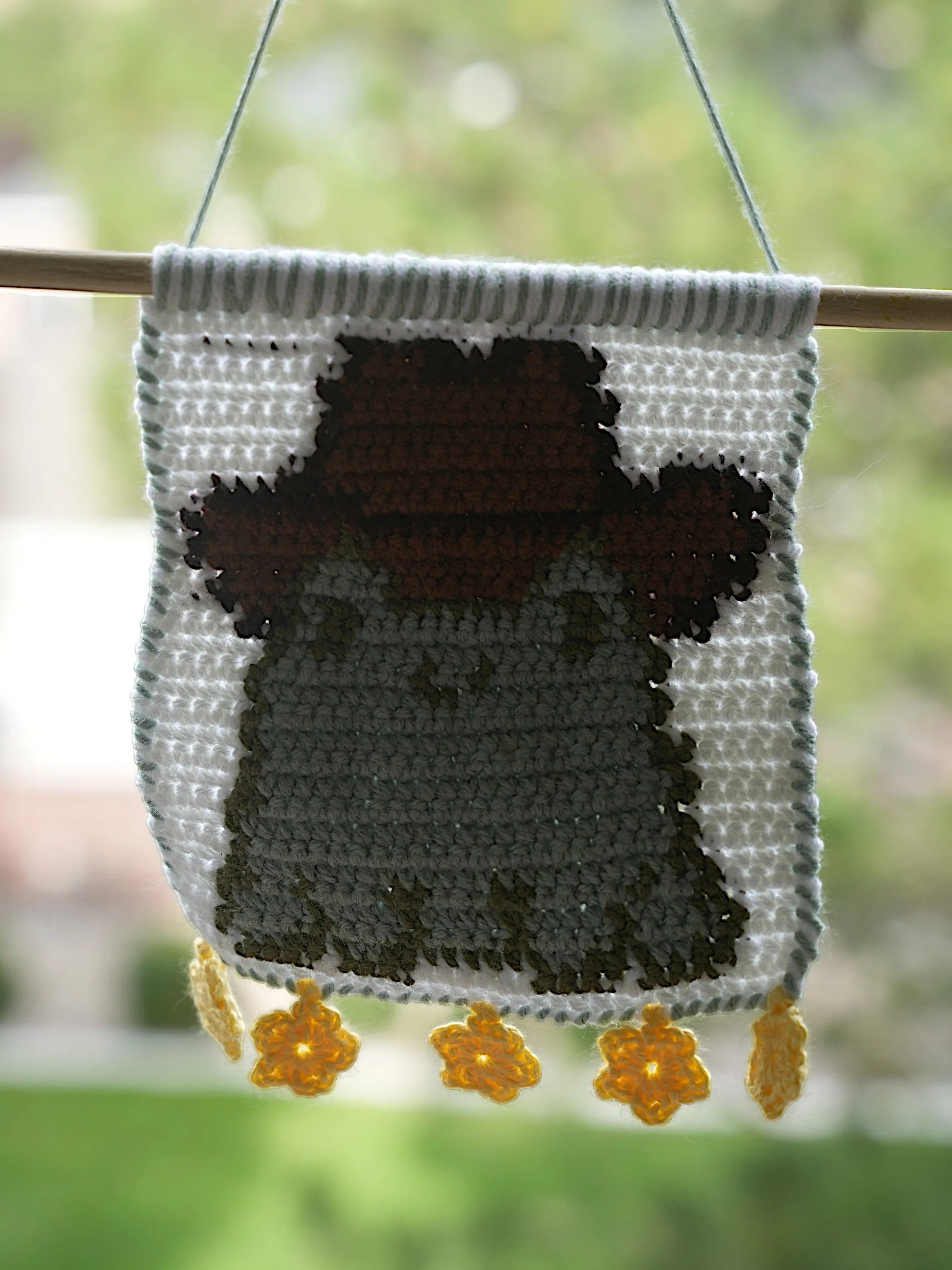 A crocheted wall hanging featuring a green frog with a brown cowboy hat, highlighted by hanging yellow star-shaped accents.