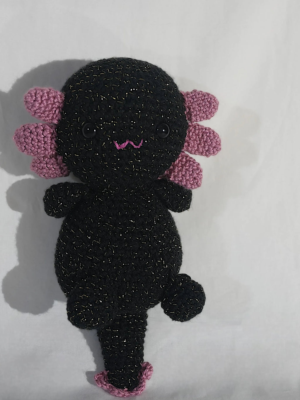 A handmade, black crocheted axolotl toy with pink gills and a playful expression.