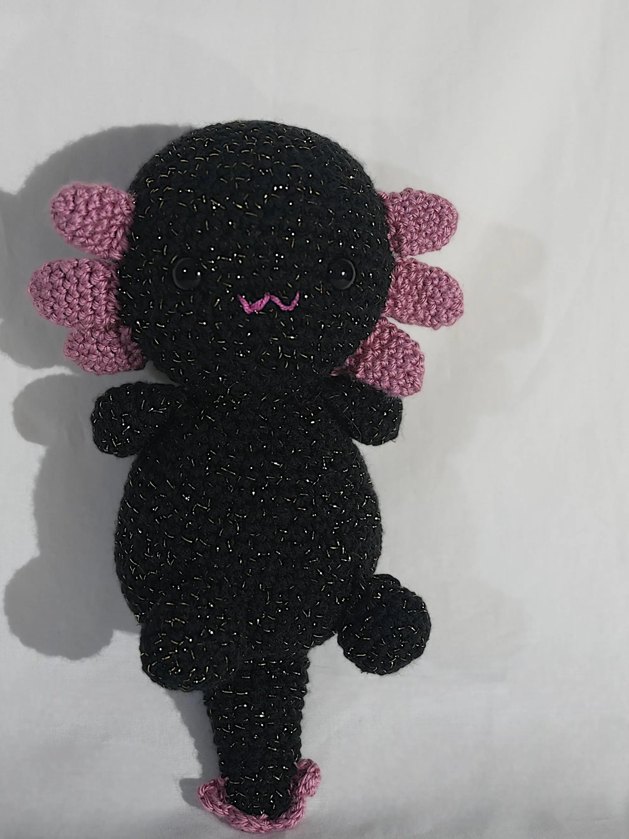 A handmade, black crocheted axolotl toy with pink gills and a playful expression.