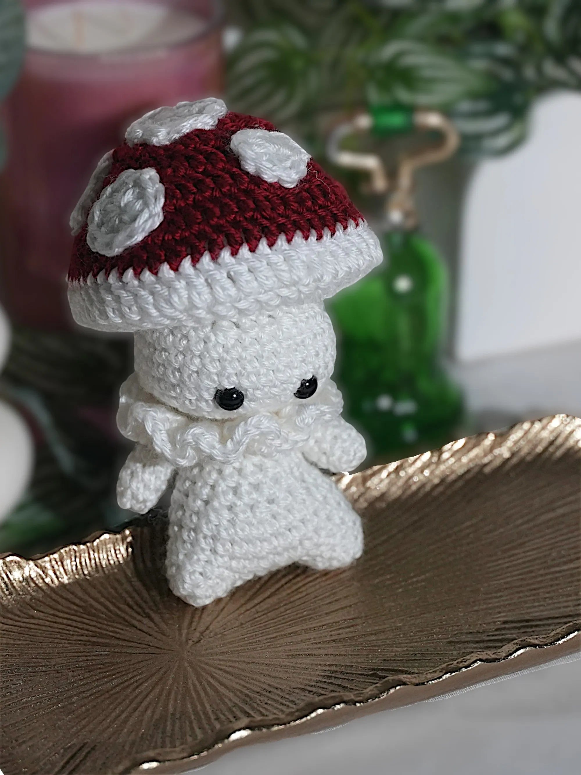 A handmade crochet doll with a white body and a red mushroom cap adorned with white spots, placed on a decorative golden tray.