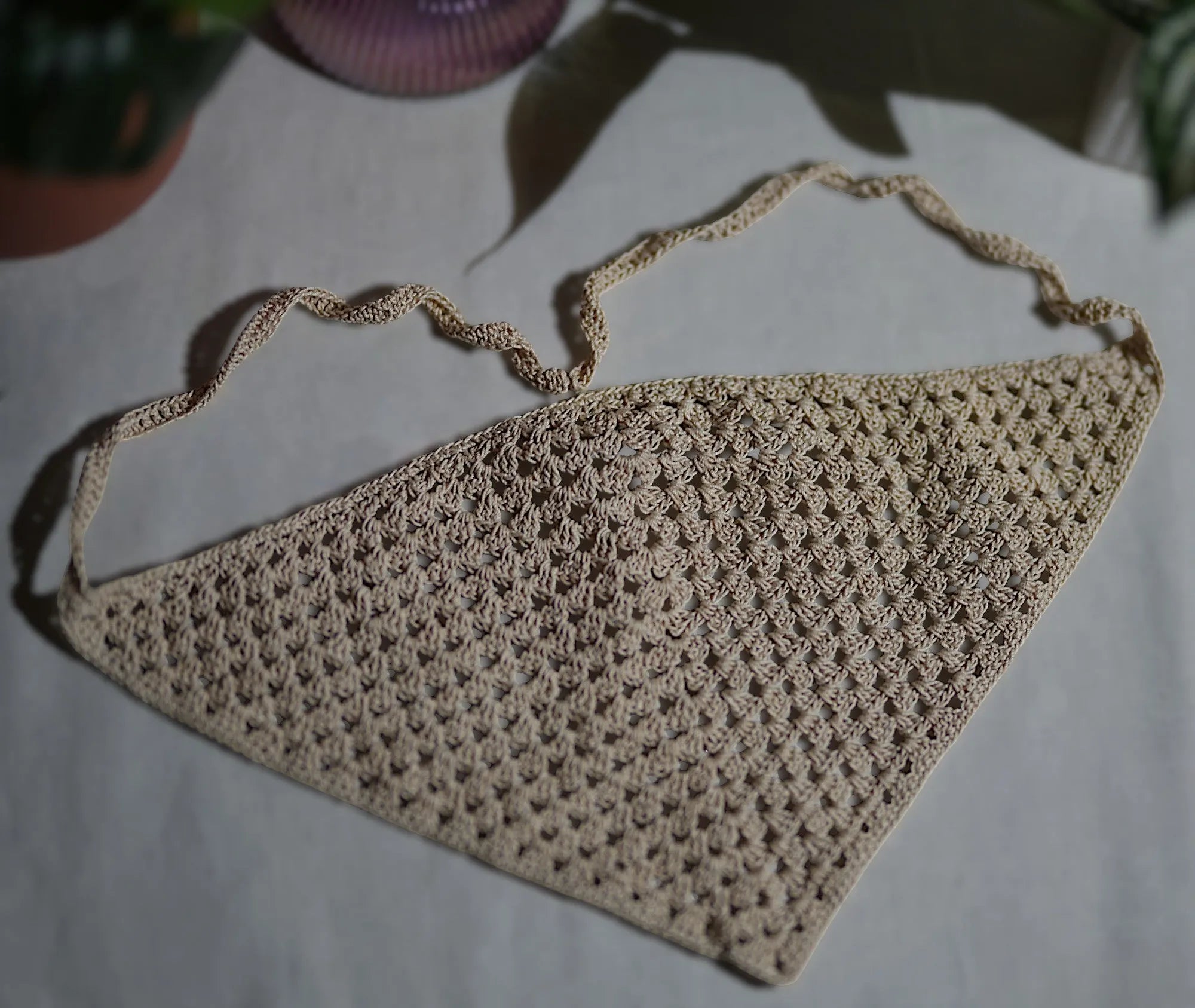 A detailed crochet headscarf laid flat, with intricate patterns and a natural beige color.