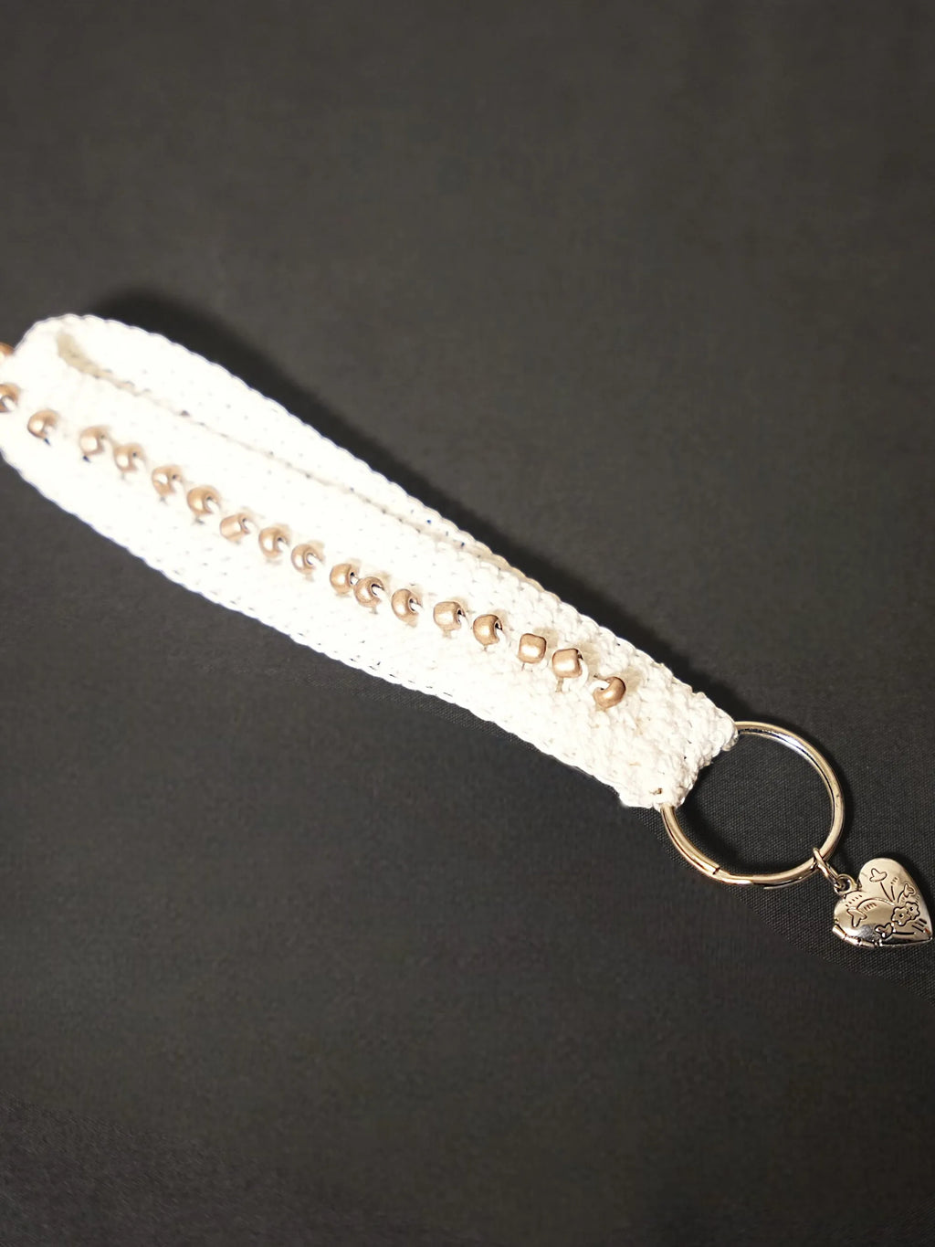 A white crochet keychain with metal bead accents and a metal ring featuring a heart-shaped charm.