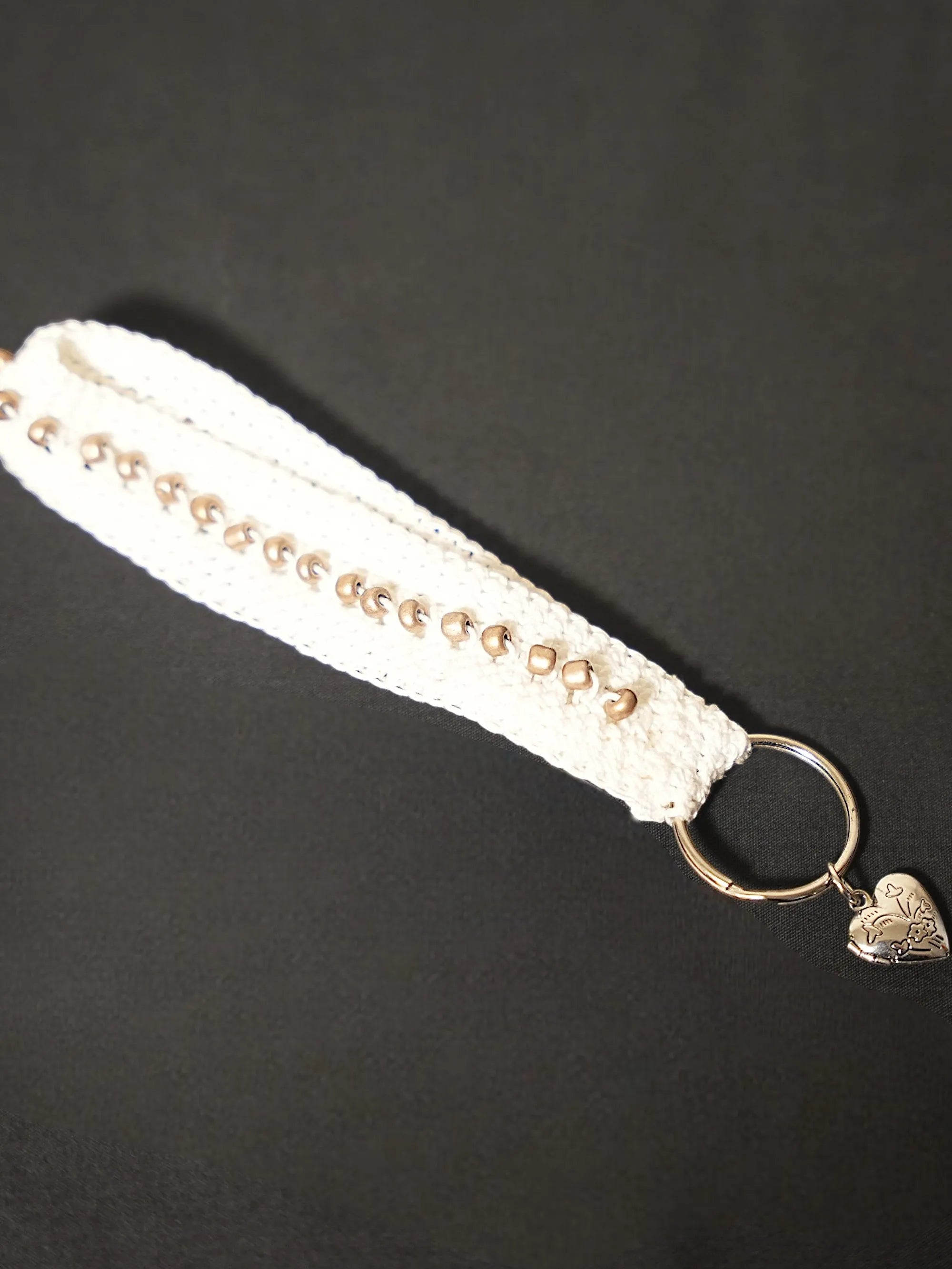 A white crochet keychain with metal bead accents and a metal ring featuring a heart-shaped charm.