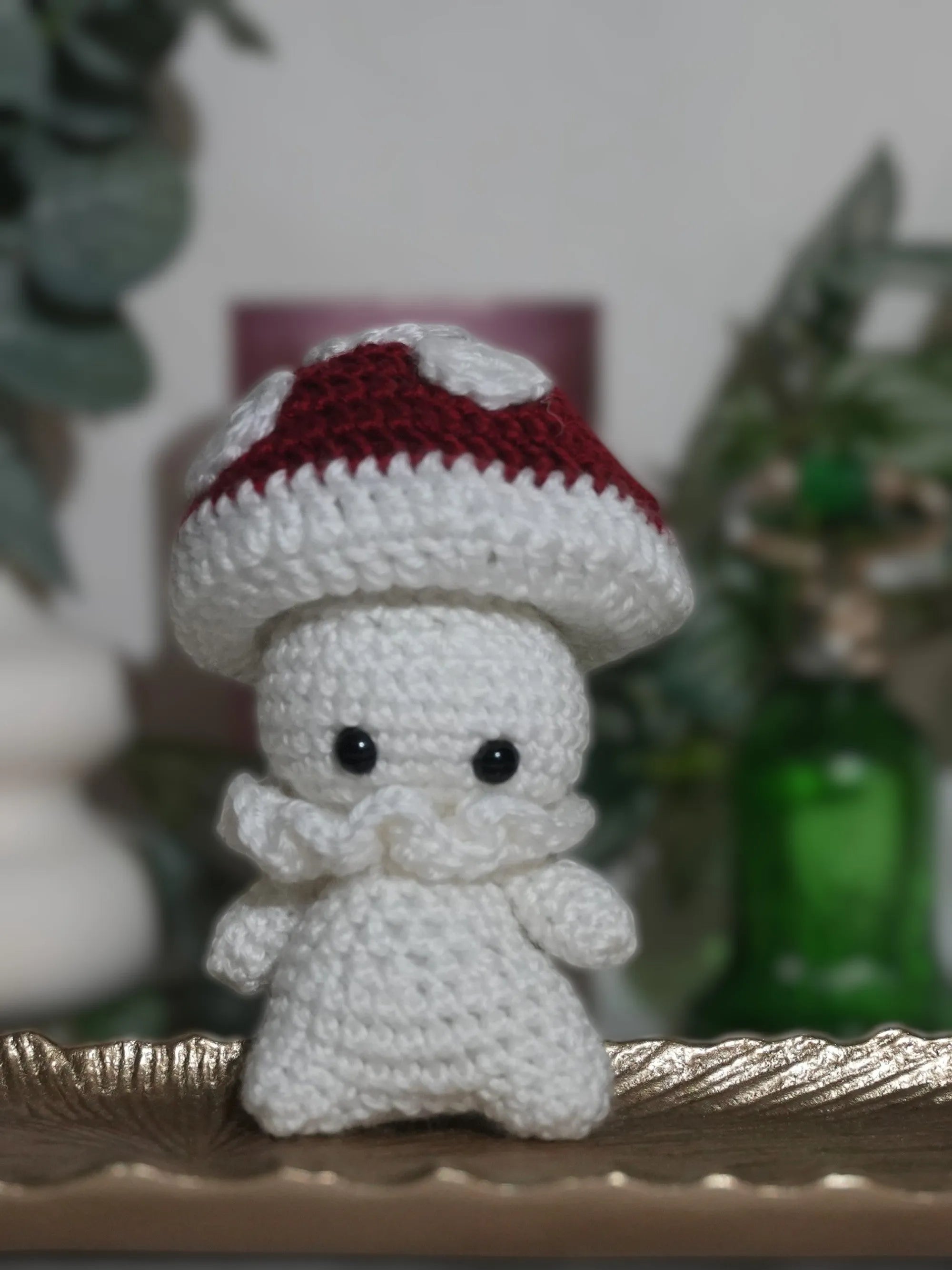 A handmade crochet doll shaped like a mushroom with a red cap and white spots, displayed on a decorative plate.