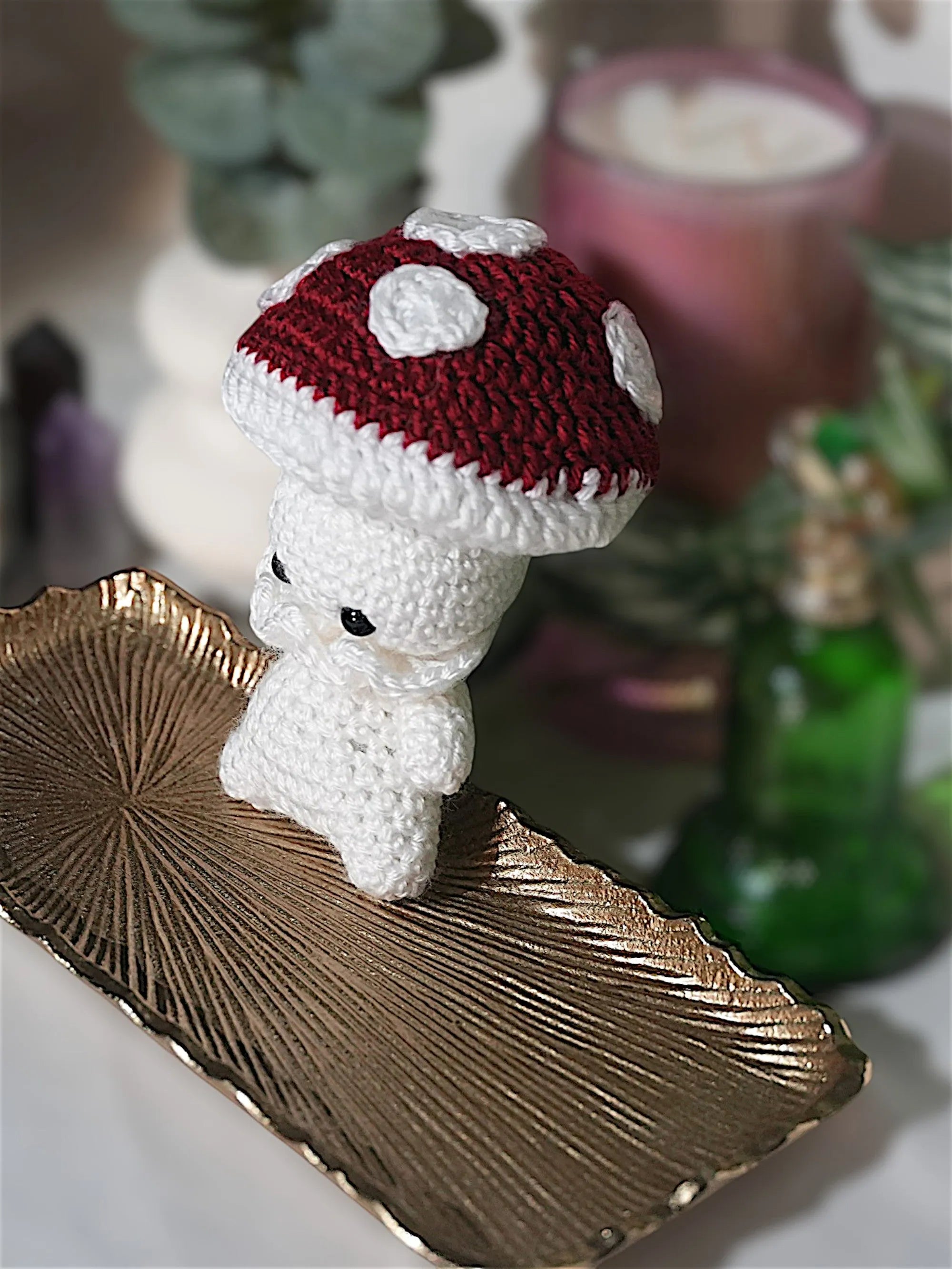 A handmade crochet toy resembling a mushroom with a red cap and white spots sitting on an ornate gold dish.