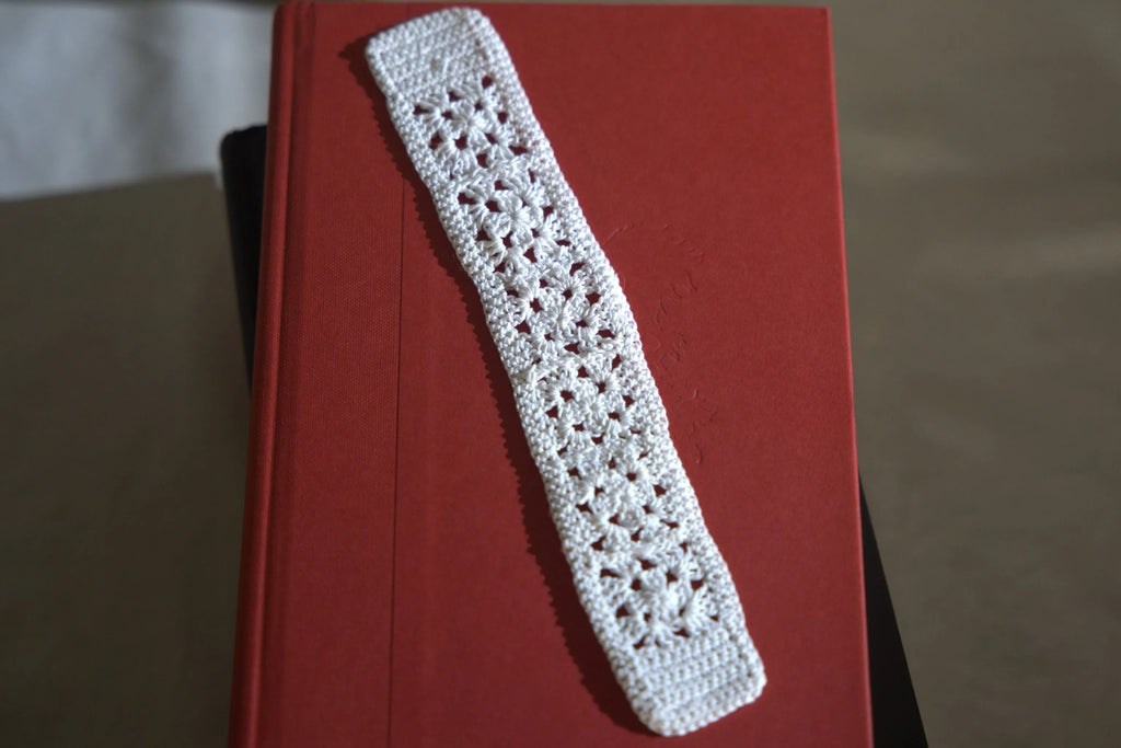 A handmade white crochet bookmark placed on a closed red hardcover book.