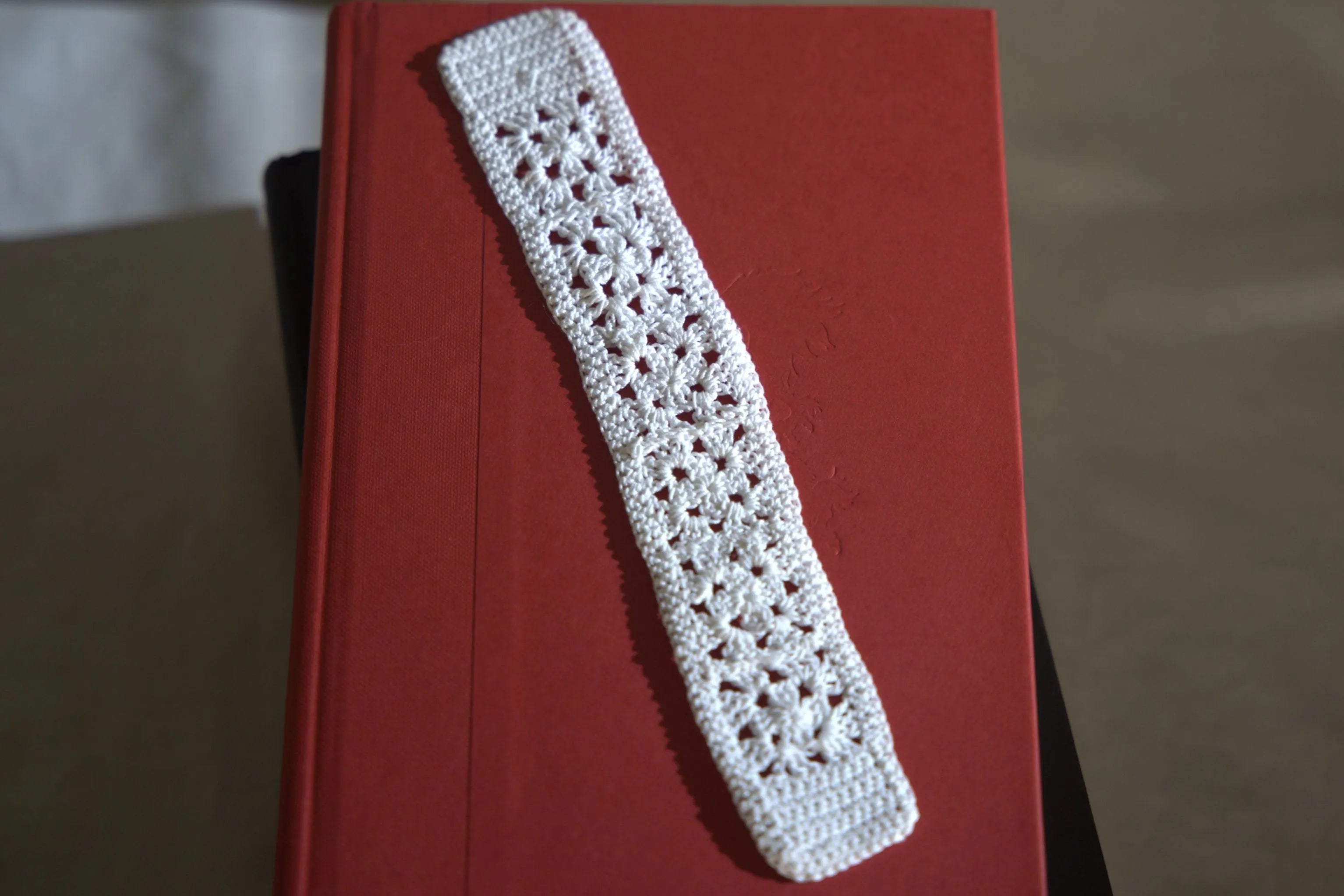 A handmade white crochet bookmark placed on a closed red hardcover book.