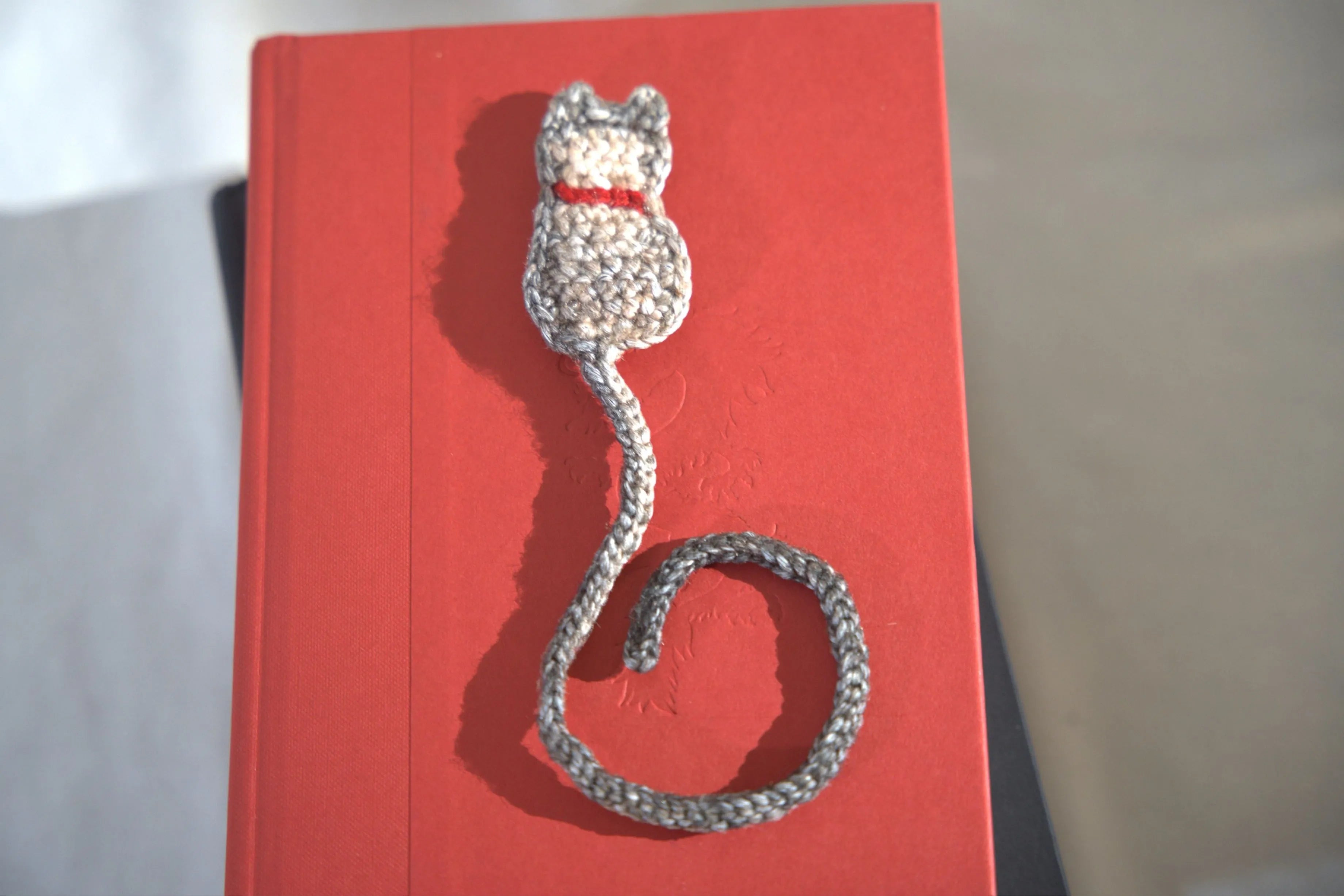 A handcrafted crocheted cat bookmark laying on a red book.