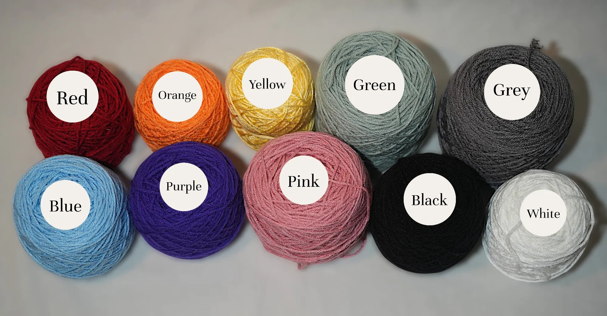 A collection of yarn bundles in various colors including red, orange, yellow, green, grey, blue, purple, pink, black, and white.