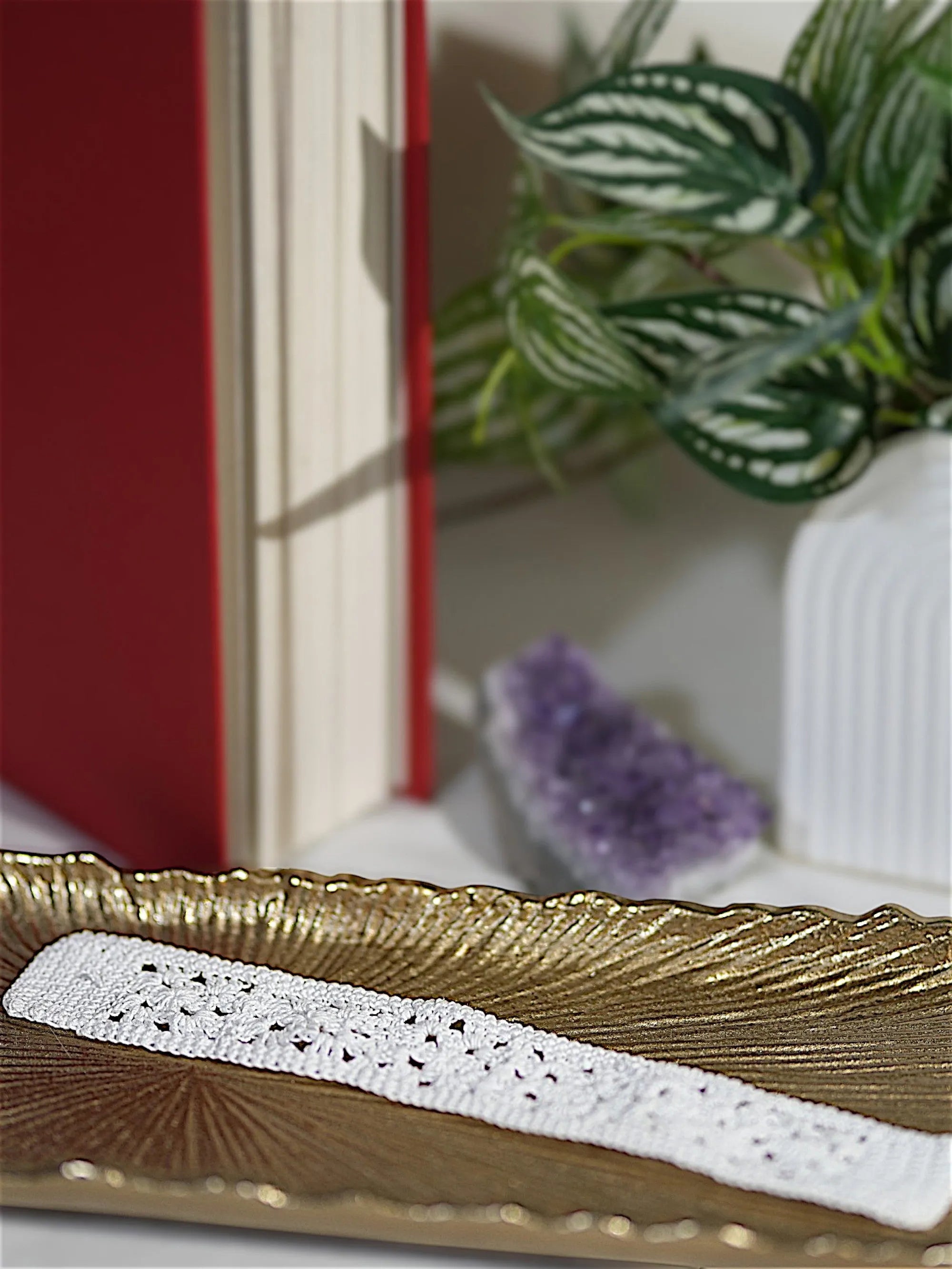 A handmade white crochet bookmark placed on a closed red hardcover book.