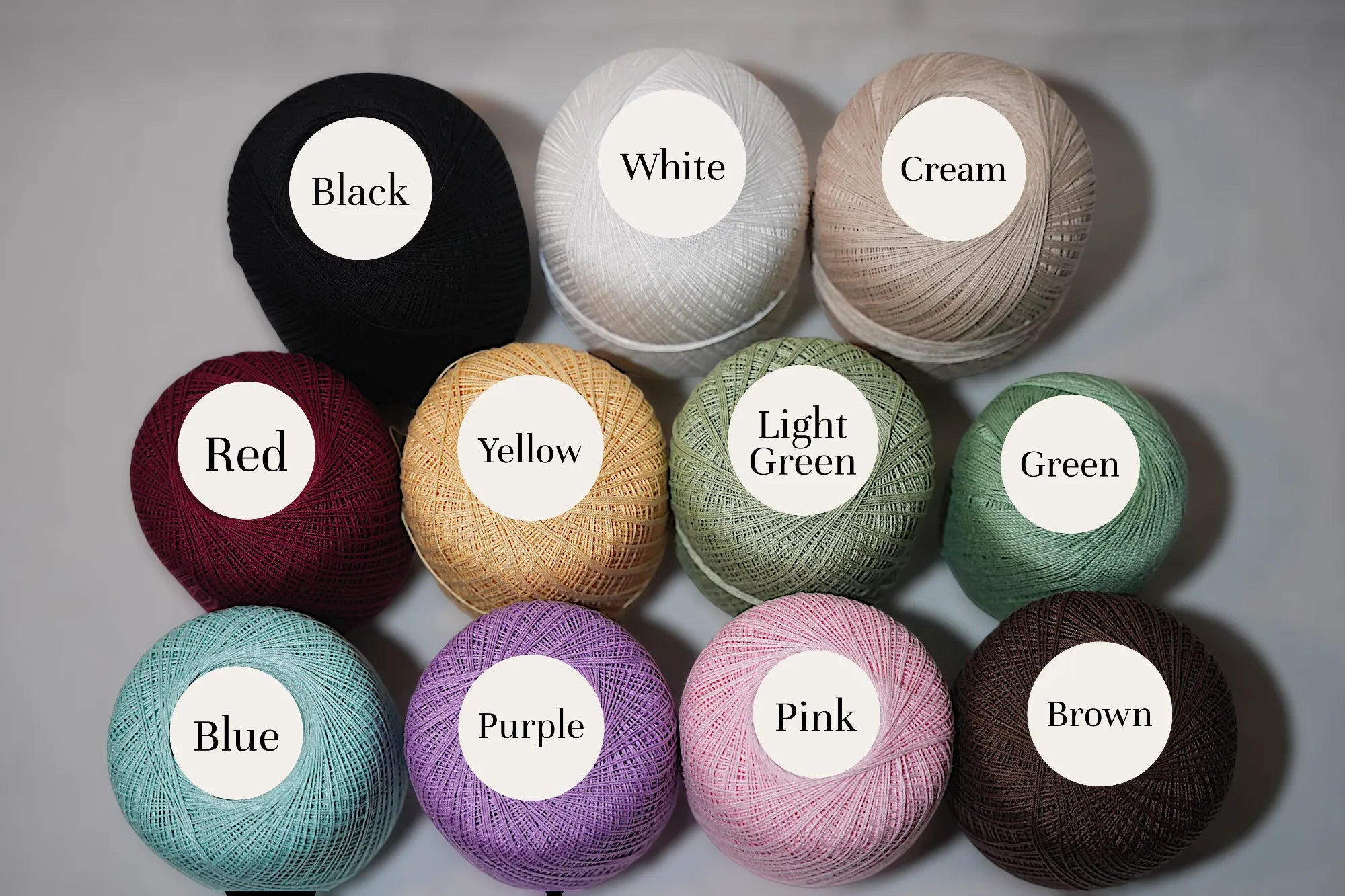 A collection of crochet thread balls in various colors including black, white, cream, red, yellow, light green, green, blue, purple, pink, and brown.